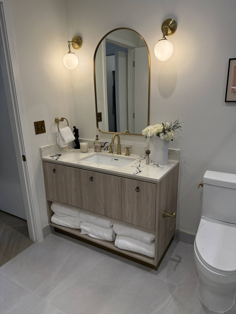 Vanity de baño con espejo oval dorado, lavamanos doble y almacenamiento de toallas en madera